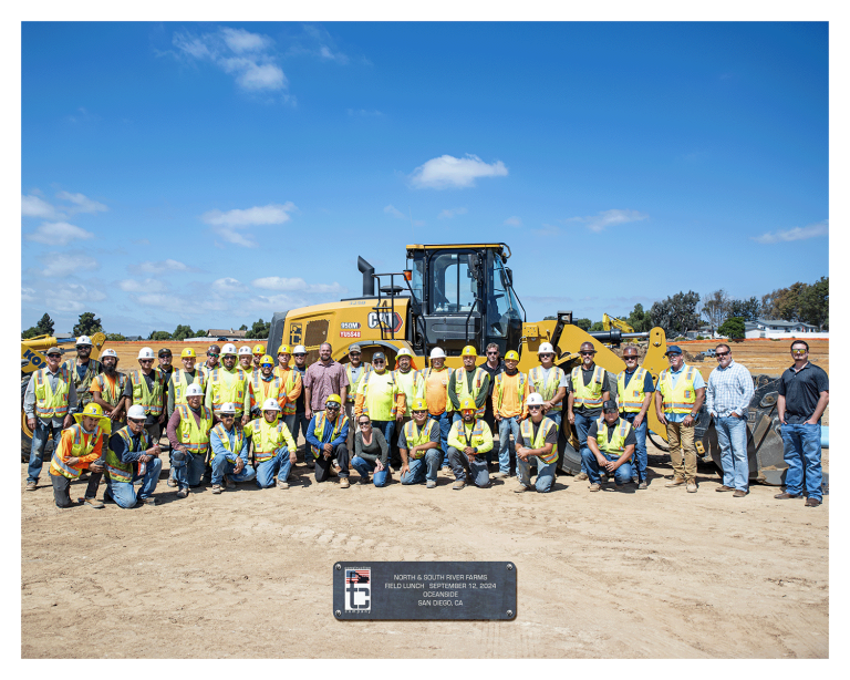 Group of 38 employees gathered for Field Lunch photo in front of loader machine